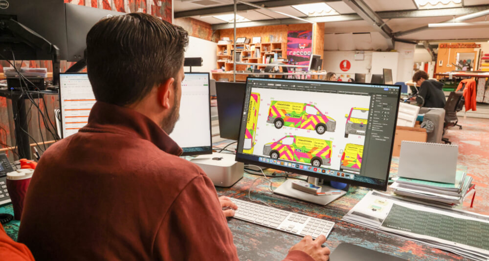 A Raccoon staff member working on a 2D vehicle template for a van wrap design, with yellow and pink details