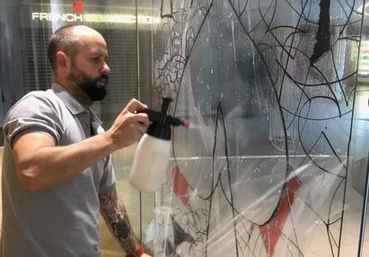 A Raccoon team member installing window graphics for Vivienne Westwood on a store window, with water bottle in action.